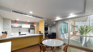 Una cocina moderna con armarios blancos, una pared de acento amarilla y un comedor con una mesa redonda y sillas de madera.