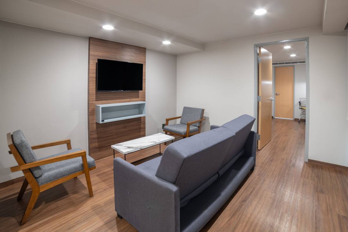 Una sala de estar moderna con un sofá gris, sillas de madera, un televisor de pantalla plana montado en un panel de madera y piso de madera.