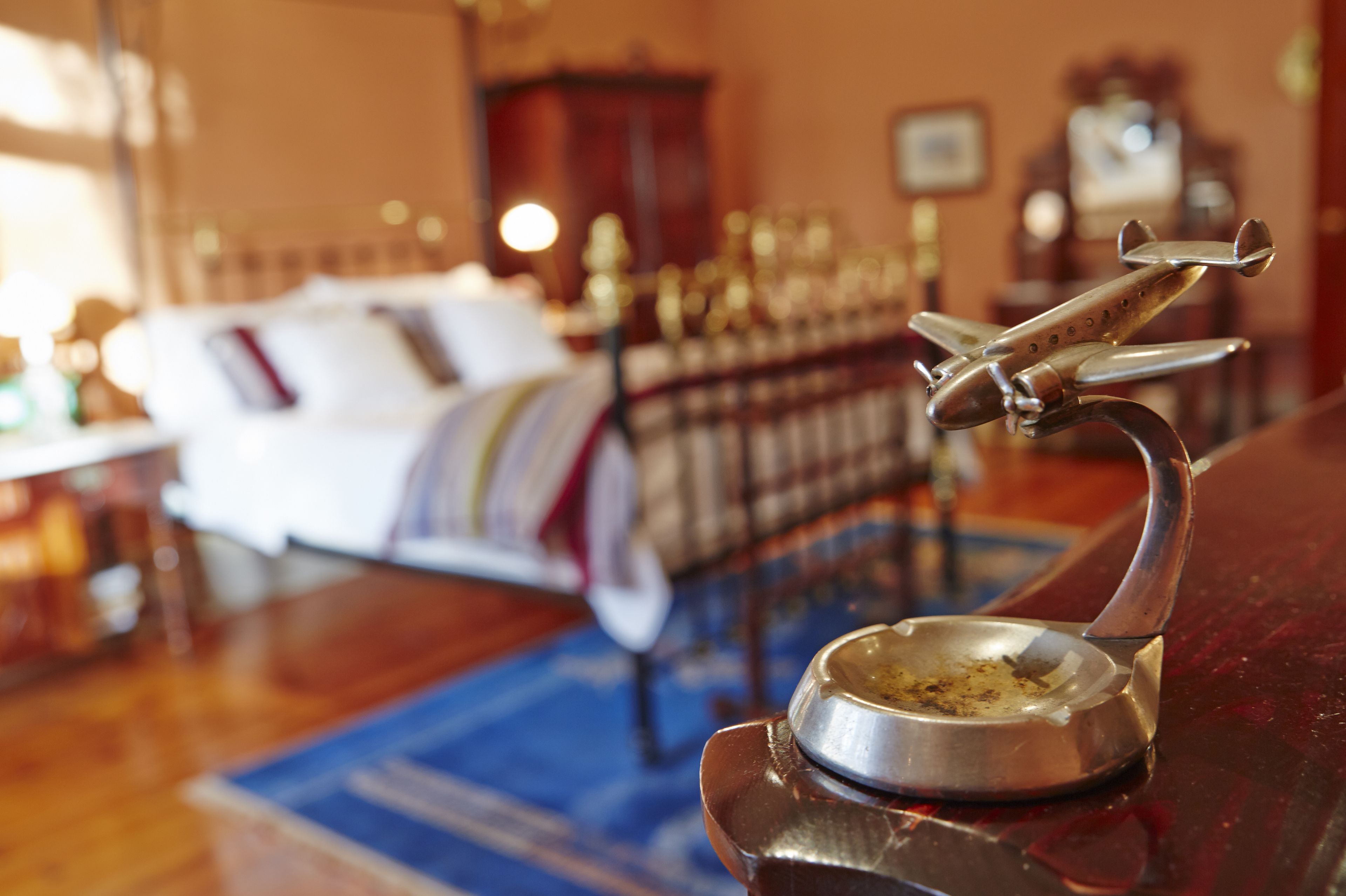 A room with a bed, a metal airplane decoration, and a small metal bowl on a stand.