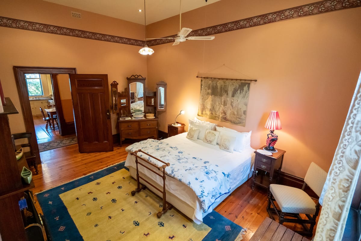 A bedroom with a bed, bedside table, lamp, chair, and a mirror.