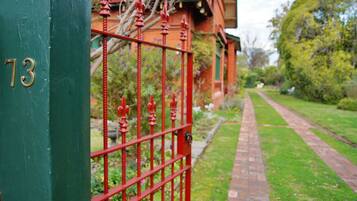 A green metal gate with the number 73, a brick pathway, and a brick building with a red roof in the background.