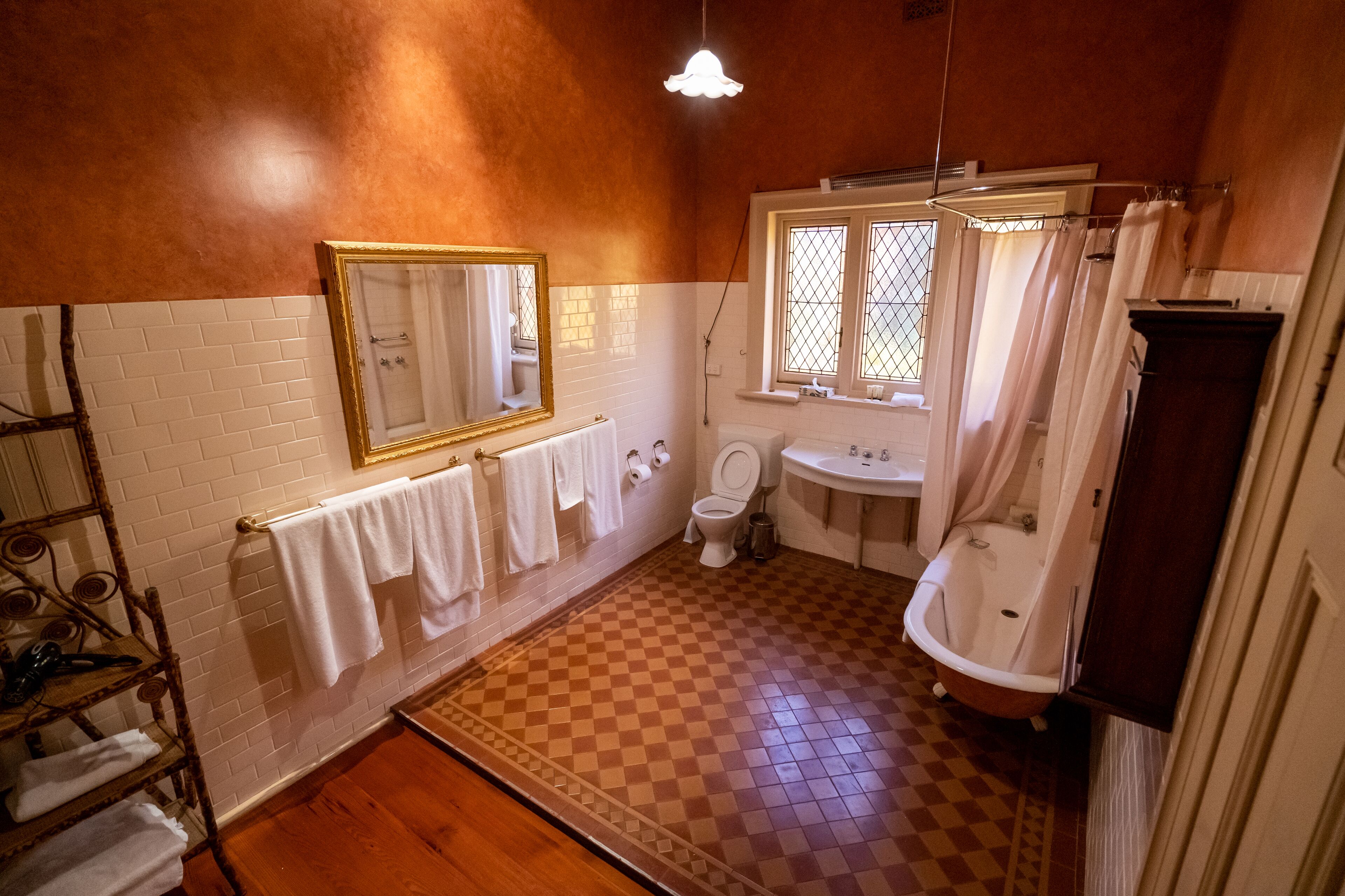 Un baño con piso a cuadros, paredes de azulejos blancos, piso de madera, lavamanos blanco, inodoro y bañera.