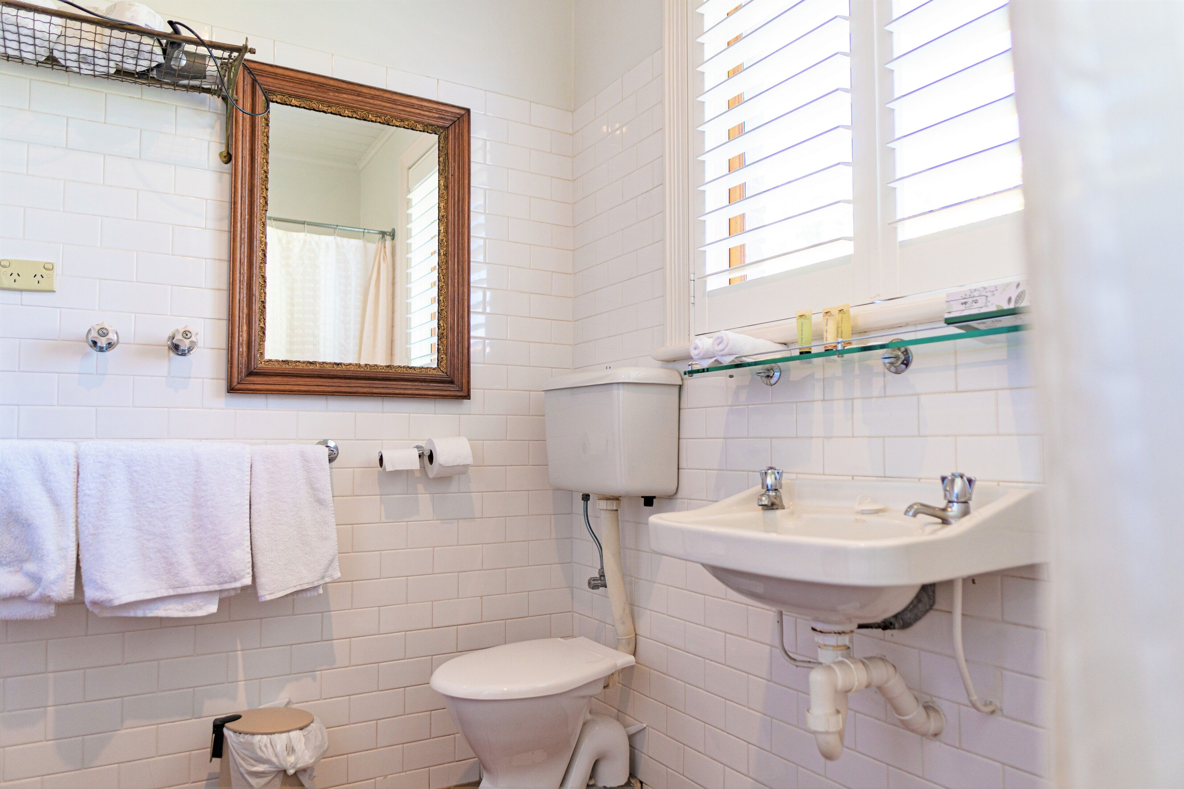 A bathroom with white tiled walls, a wooden-framed mirror, a toilet, a sink, and a towel rack.