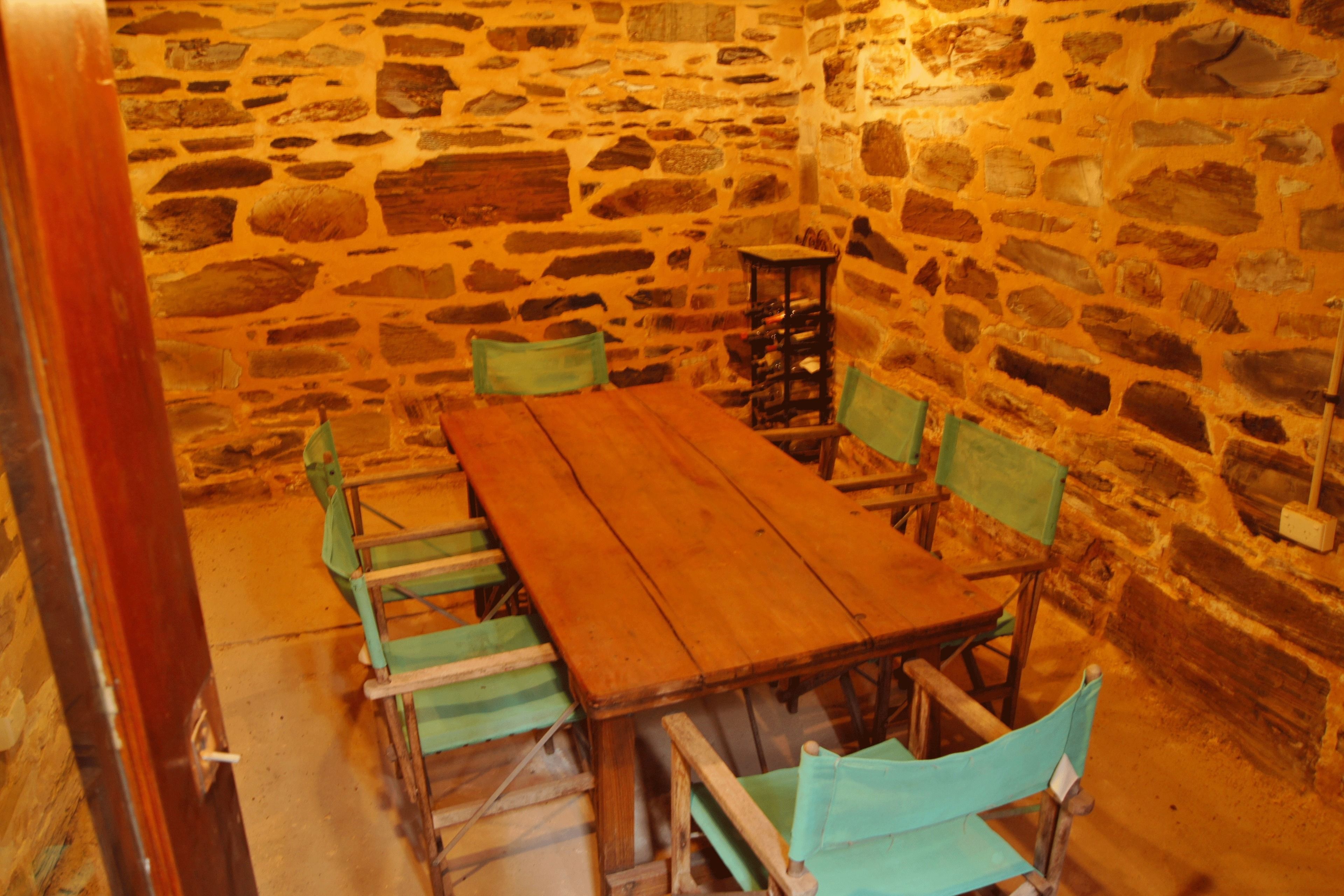 Una habitación con paredes de piedra, una mesa de madera y sillas verdes.