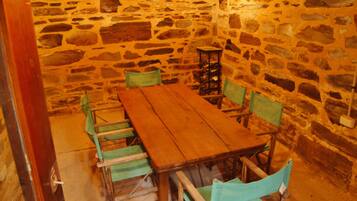 Una habitación con paredes de piedra, una mesa de madera y sillas verdes.