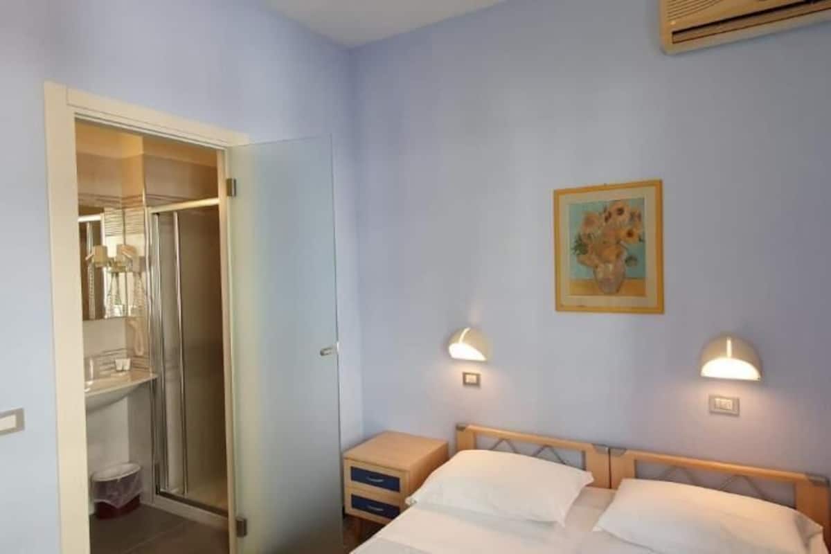 A bedroom with a bed, bedside tables, a nightstand, a closet, and two wall-mounted lamps.