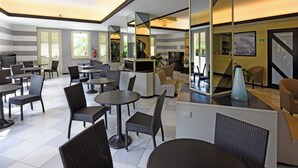 A modern indoor dining area with multiple tables and chairs, a central counter, and large mirrors on the walls.