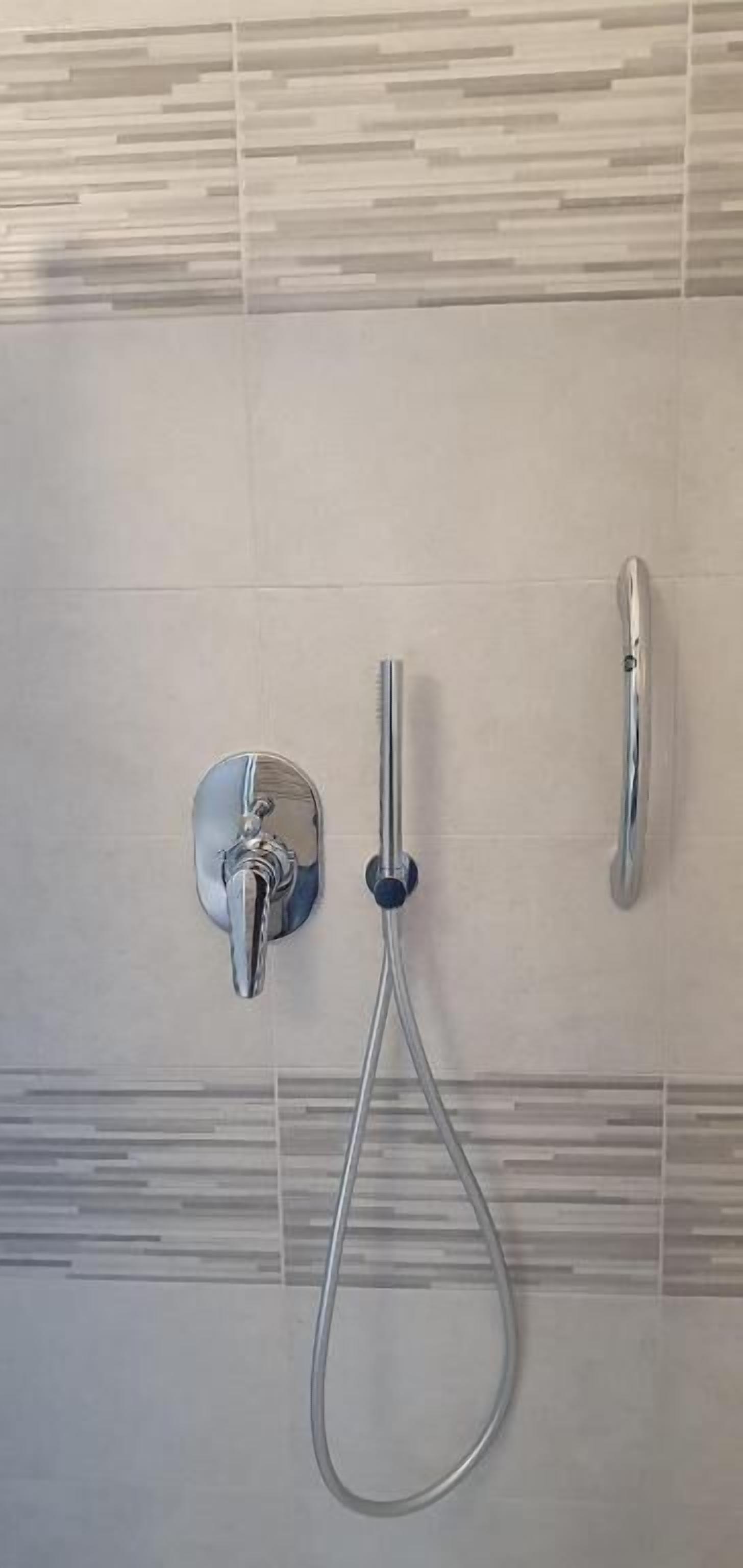 A shower with a handheld showerhead and two wall-mounted faucets.