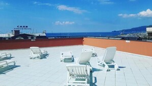 A rooftop terrace with white lounge chairs and a clear view of the sea and airport in the background.