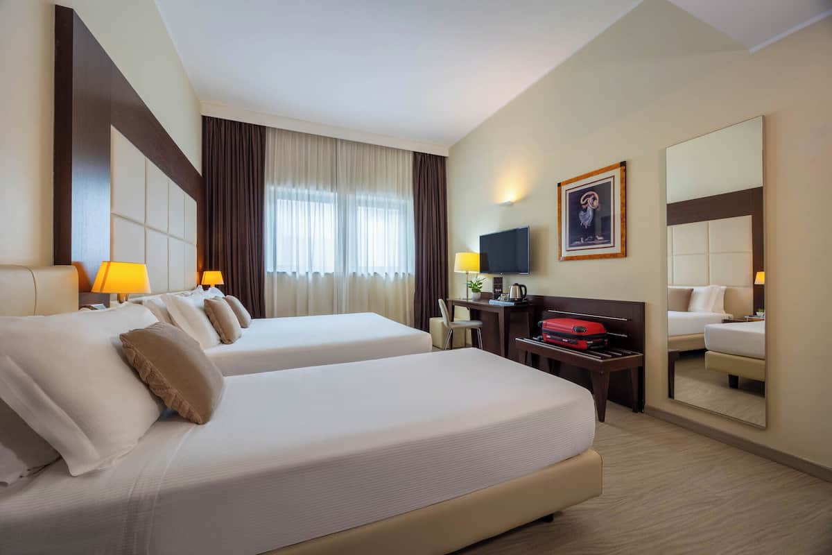 Ein Hotelzimmer mit zwei Betten, einem Schreibtisch, einem Fernseher und einem großen Spiegel.