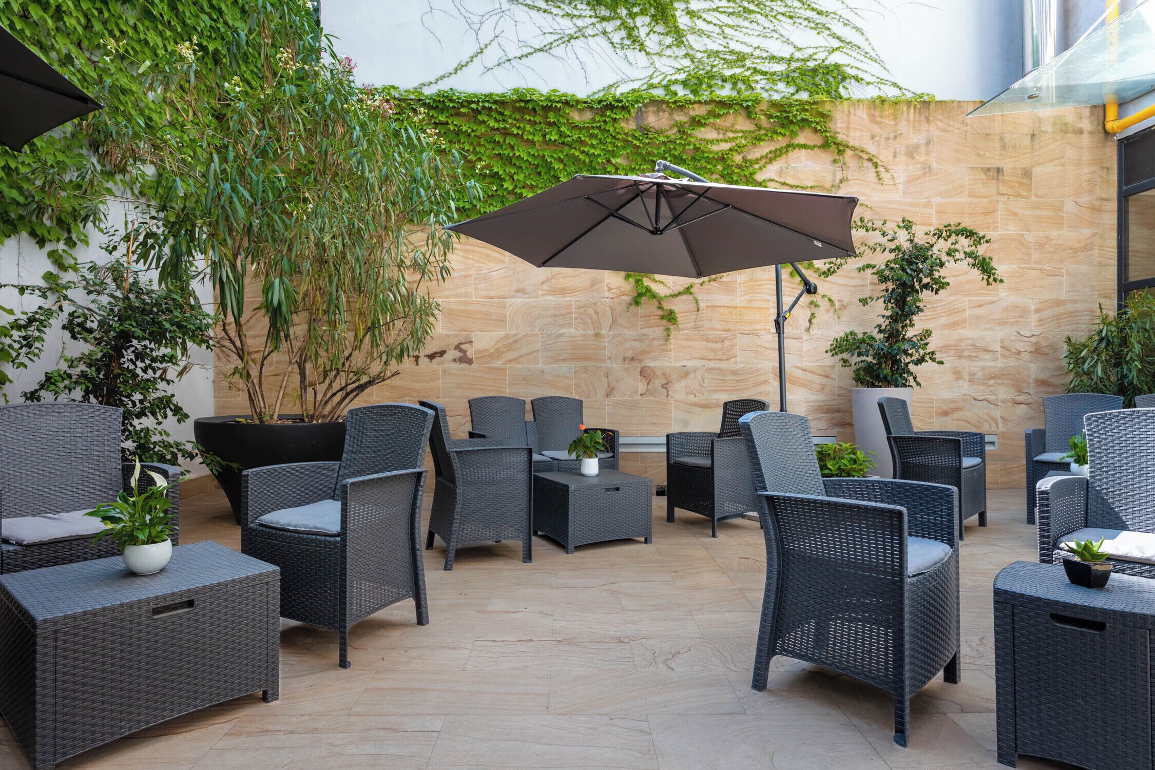 An outdoor patio with wicker furniture, a large umbrella, and potted plants.