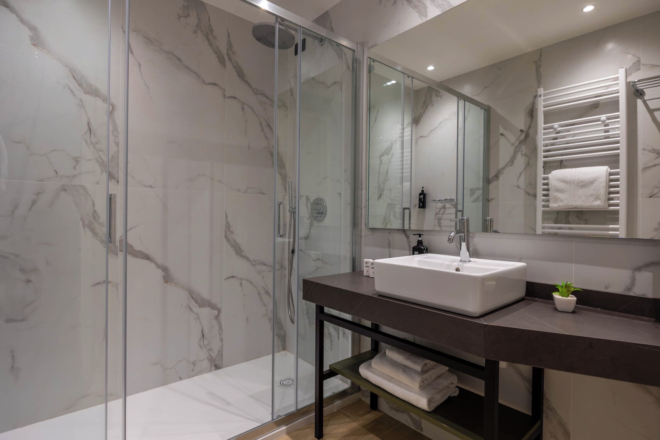 A modern bathroom with a glass-enclosed shower, a marble backsplash, a white sink, and a towel rack.