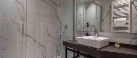 A modern bathroom with a glass-enclosed shower, a marble backsplash, a white sink, and a towel rack.