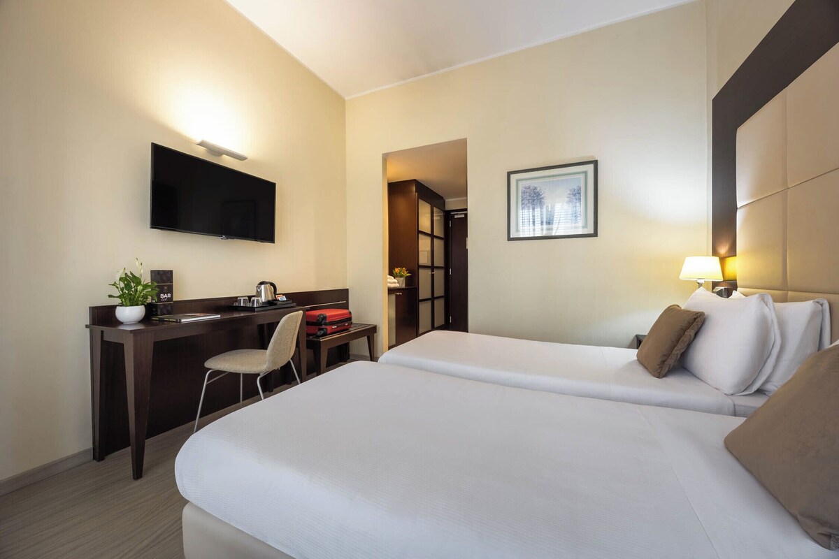 A hotel room with a bed, a desk, a chair, a television, and a framed picture on the wall.