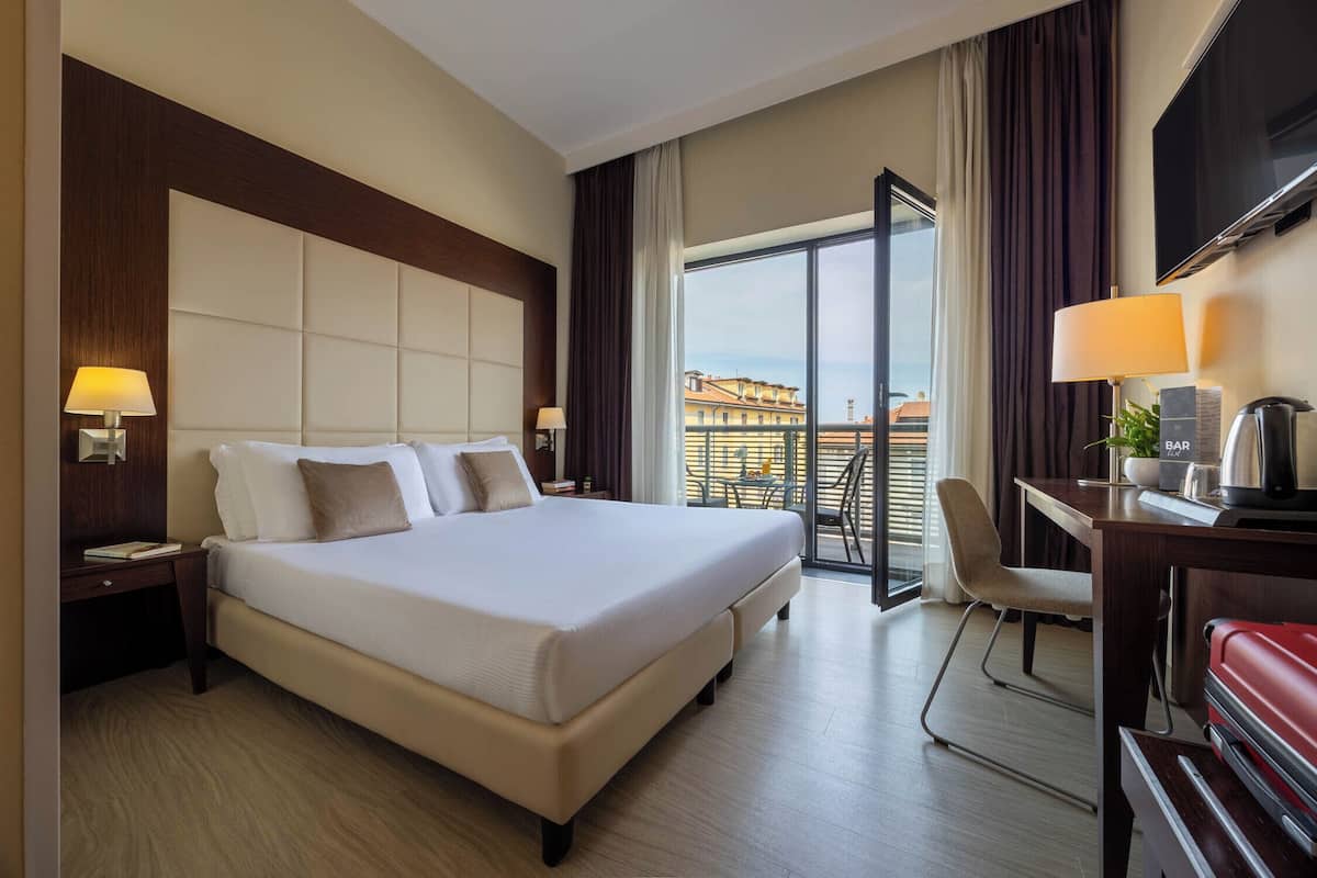 Ein Hotelzimmer mit einem großen Bett, einem Schreibtisch mit Stuhl, einem Fernseher und einem Balkon mit Aussicht.