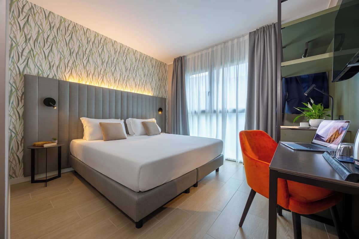 Ein modernes Hotelzimmer mit einem großen Bett, einem Schreibtisch mit einem Laptop und einem Sessel.