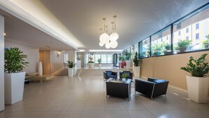 Eine geräumige Lobby mit moderner Möblierung, großen Fenstern und Zimmerpflanzen.