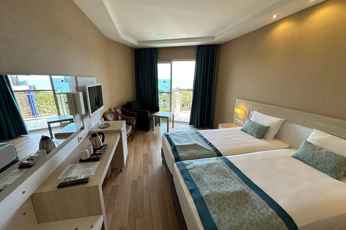A hotel room with two beds, a desk with a TV, and a view of the sea.