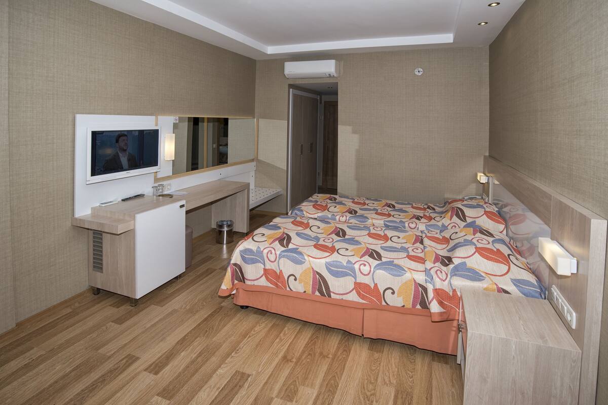 A hotel room with a bed, a desk, a TV, and an air conditioning unit.