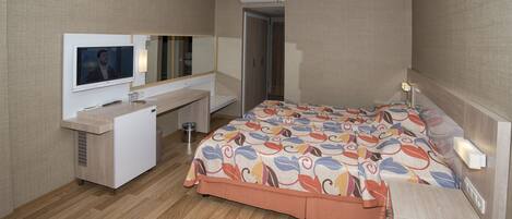 A hotel room with a bed, a desk, a TV, and an air conditioning unit.