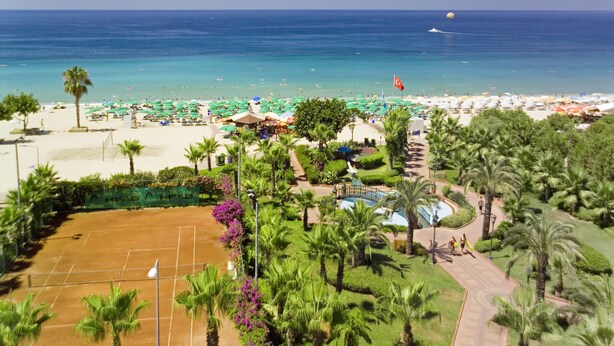 Un resort en la playa con cancha de tenis, palmeras y vista al océano.