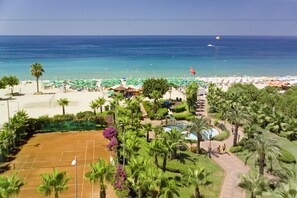 Un resort en la playa con cancha de tenis, palmeras y vista al océano.