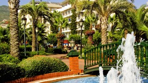 Una piscina con una fuente, rodeada de palmeras y un paseo de ladrillo.