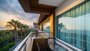 Un balcón con mesa y sillas, con vista a una zona costera con palmeras y el mar.