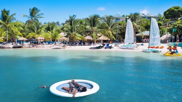 Una playa con agua azul cristalina, sillas de descanso y palmeras.
