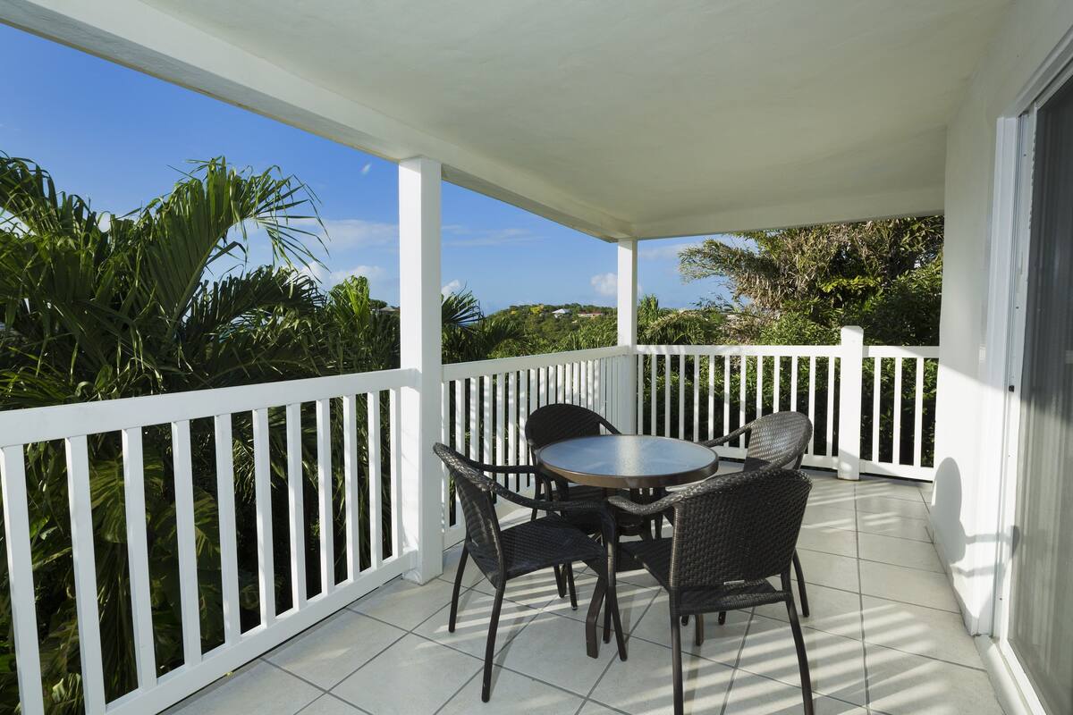 A covered patio with a white railing, a round table, and four chairs.
