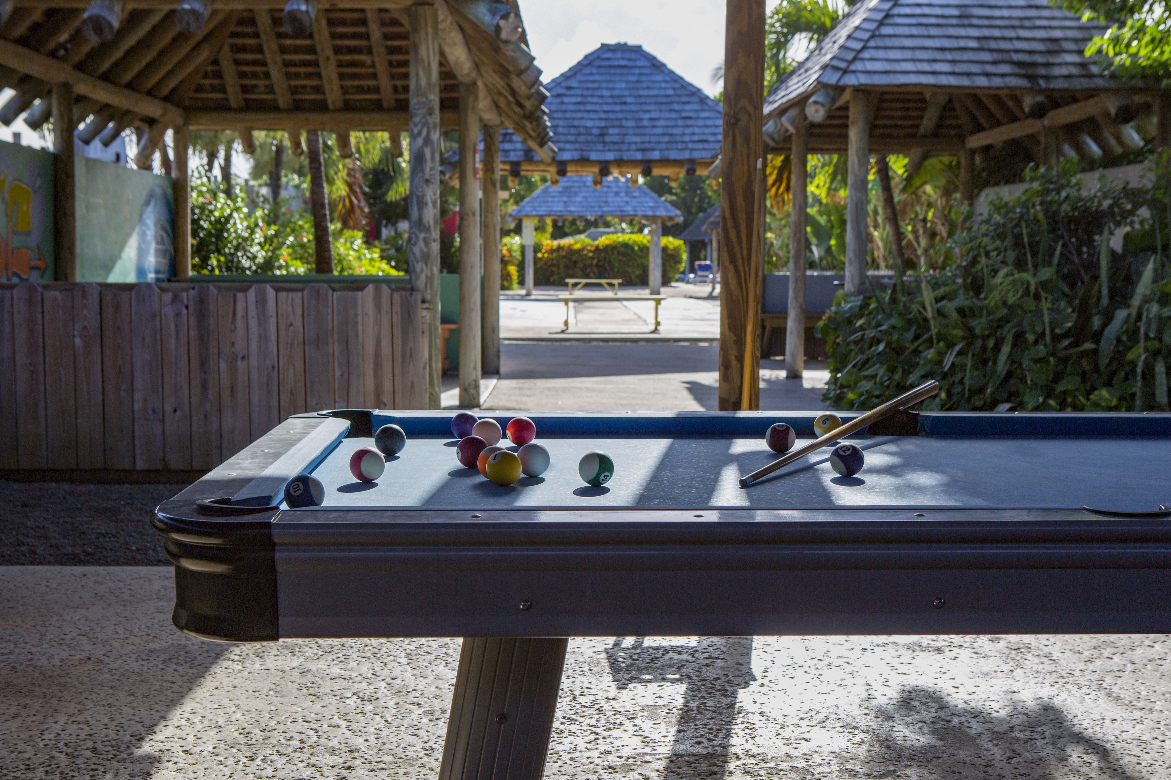 Une table de billard avec des billes, entourée de structures en bois et de verdure.