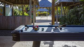 Une table de billard avec des billes, entourée de structures en bois et de verdure.
