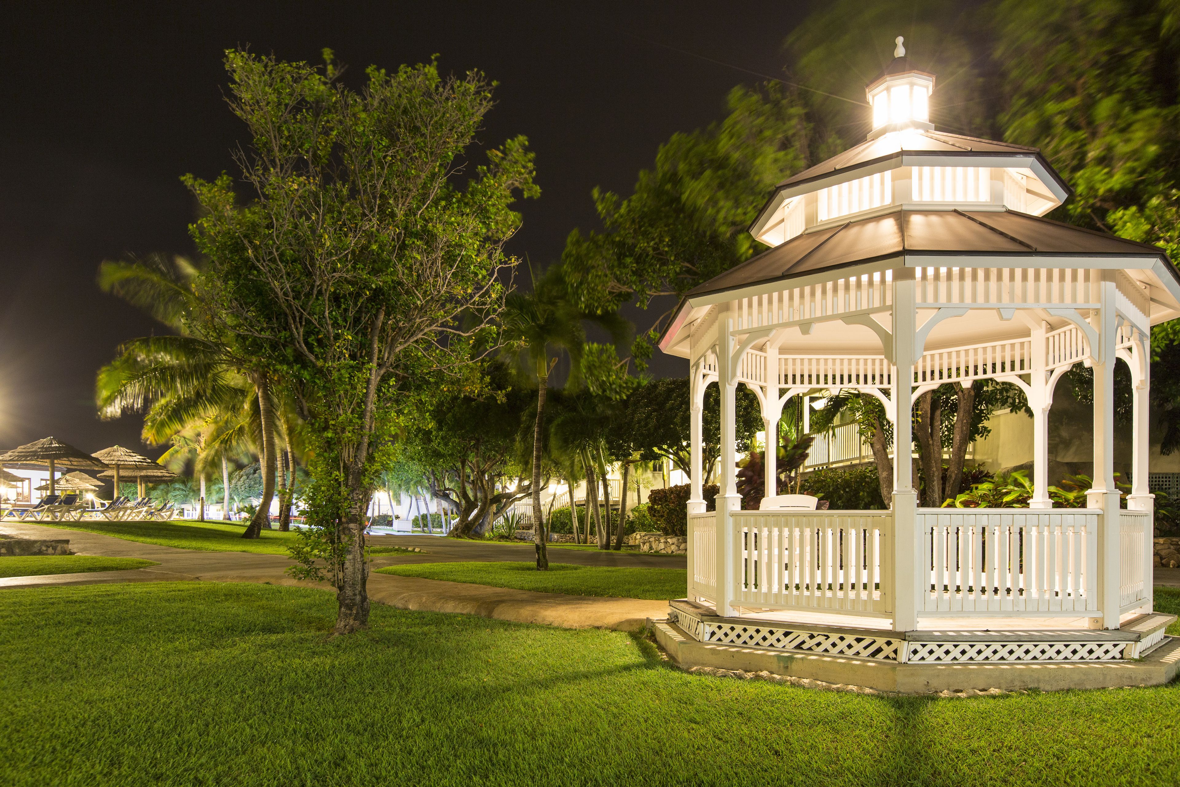 Un kiosque blanc avec un toit, entouré d’herbe et d’arbres, de nuit.