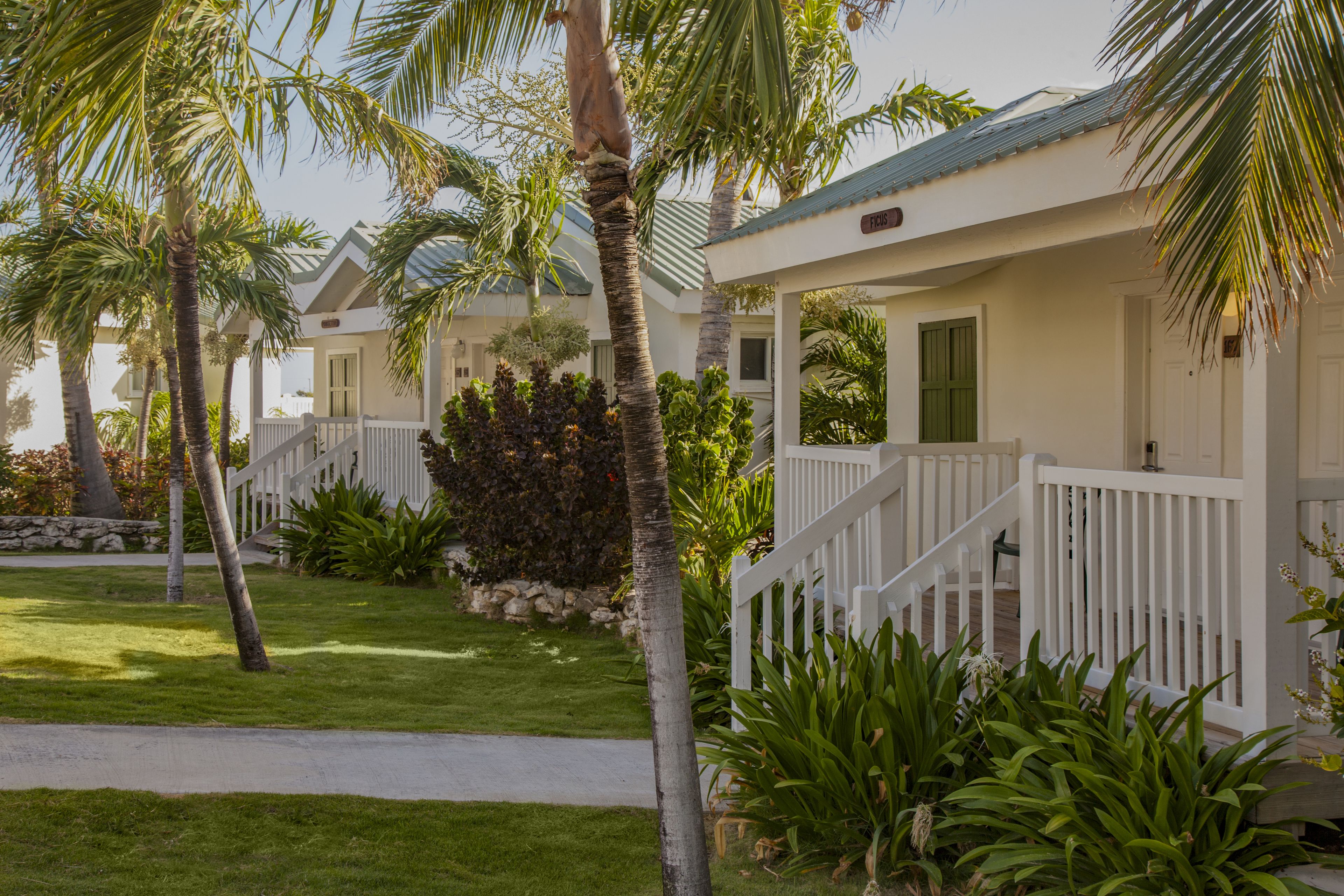 A beachfront property with white buildings, palm trees, and a well-maintained lawn.