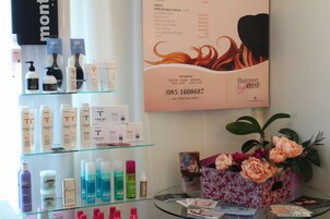 Interior de salón de belleza con diversos productos para el cuidado del cabello en estanterías y un cartel publicitario de servicios.