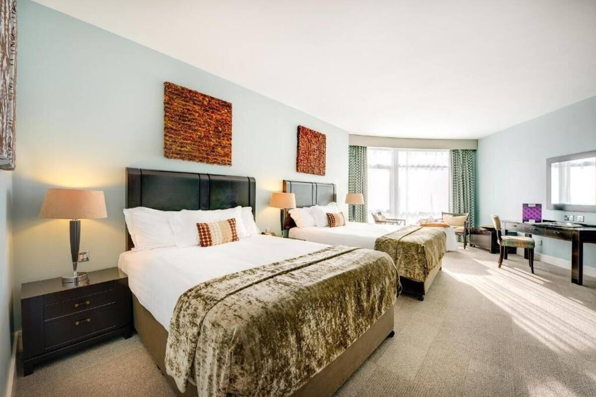A hotel room with two beds, a desk, a chair, and a television.