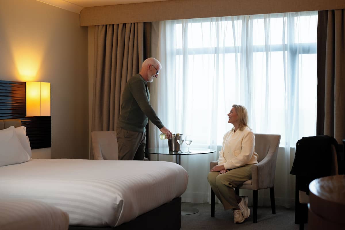 A hotel room with a bed, a sitting area with a table, and a window with curtains.