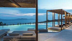 An infinity pool with lounge chairs and a wooden pergola overlooking a body of water. - Rocabella Mykonos Hotel, a member of Design Hotels (Mykonos)