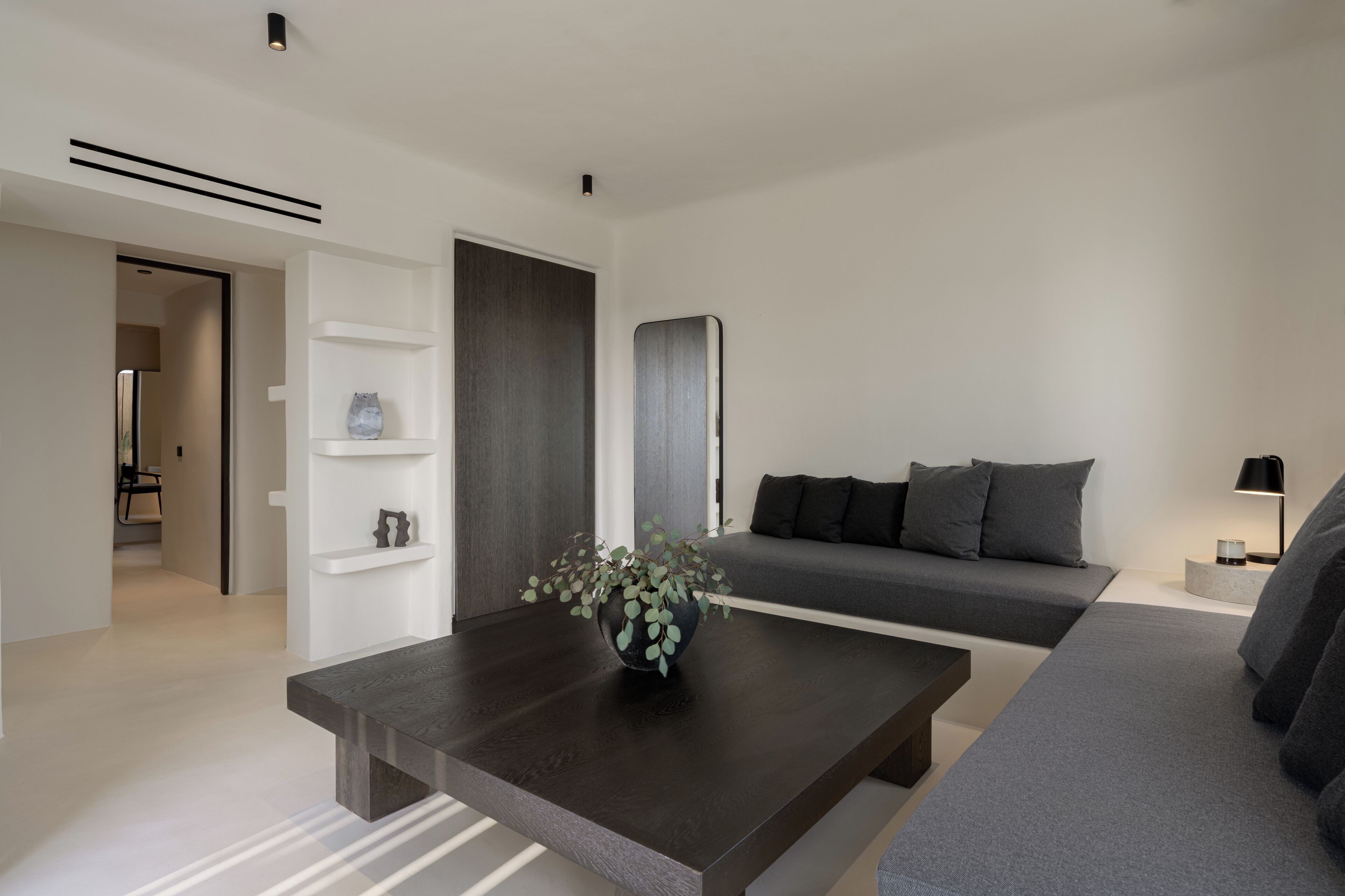 Un salón moderno con una mesa de centro de madera oscura, un sofá gris y un estante blanco.