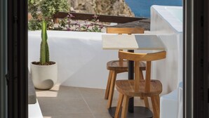 Een balkon met een tafel en stoelen, een cactus in een pot, en uitzicht op zee en verre gebouwen.