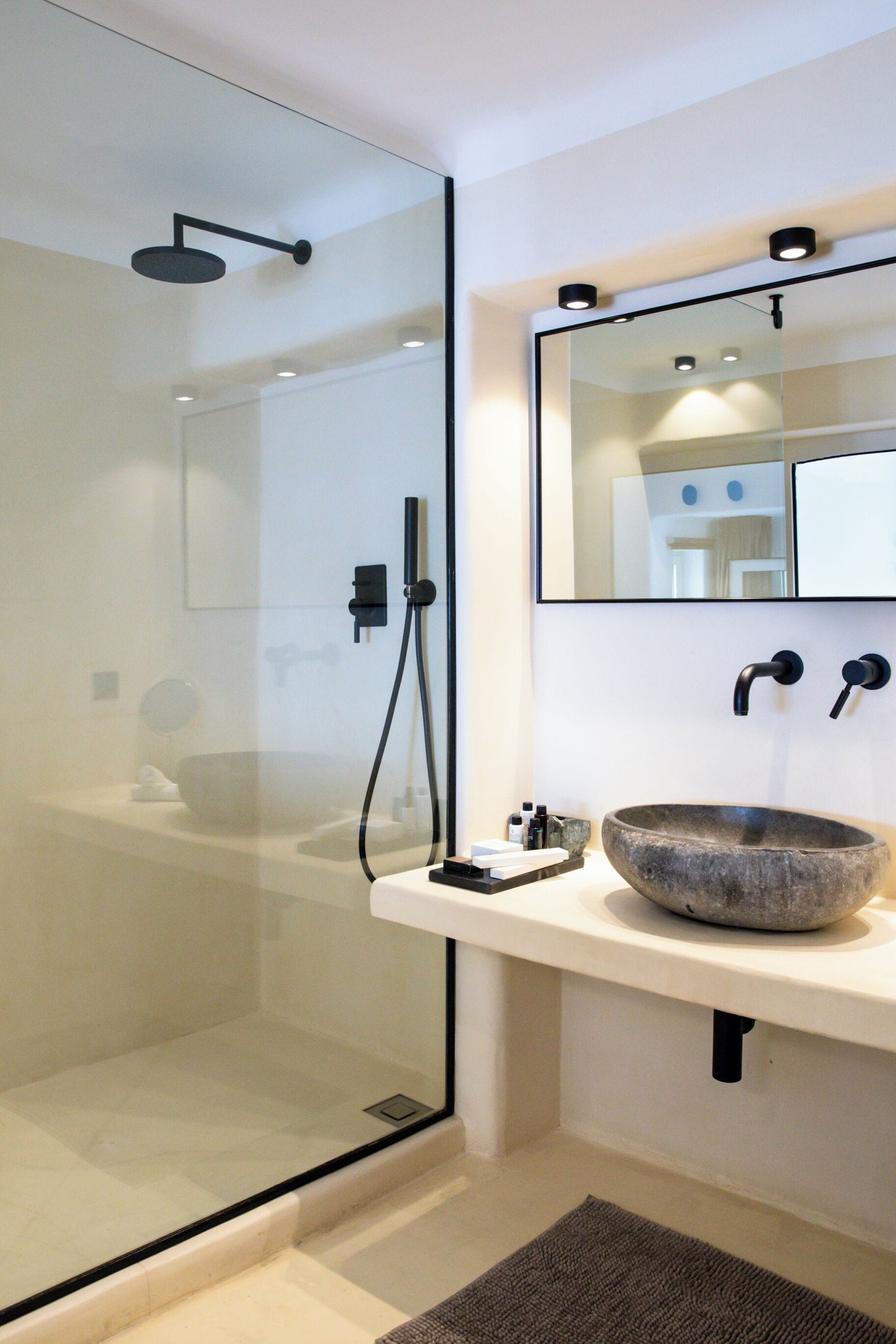 Un baño moderno con cabina de ducha de vidrio, un lavamanos grande de piedra y un espejo sobre el lavamanos.