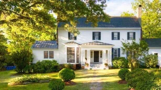 A two-story white house with a front porch, surrounded by lush greenery. - Oak Grove Bed and Breakfast (South Boston)