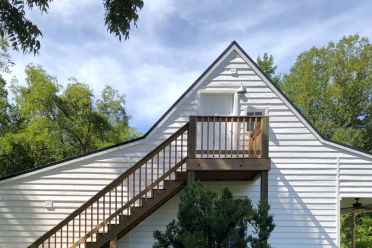 A white building with a wooden staircase leading to a balcony.