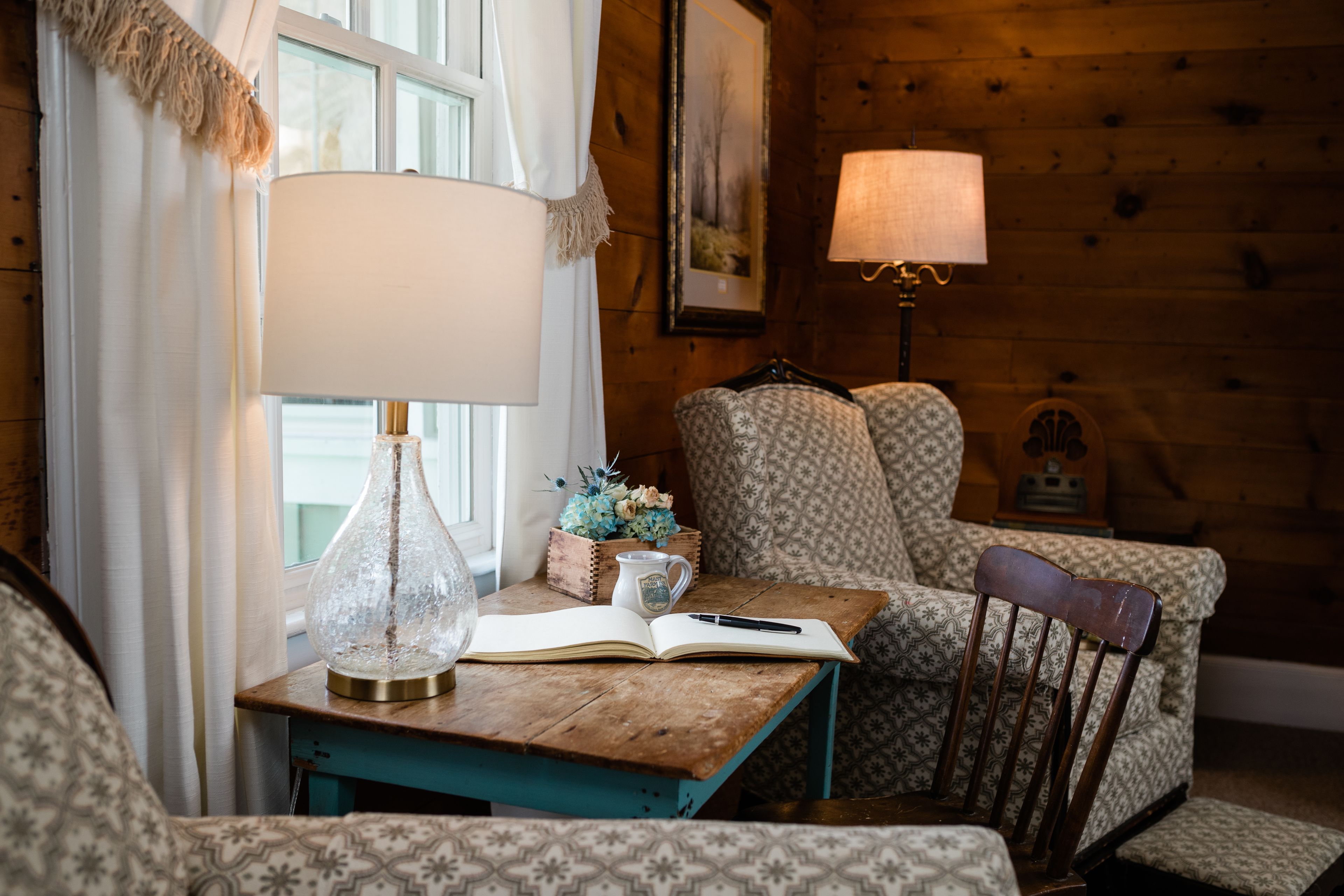 A cozy room with a wooden wall, a table with a lamp, a chair, and a book.