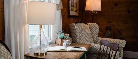 A cozy room with a wooden wall, a table with a lamp, a chair, and a book.