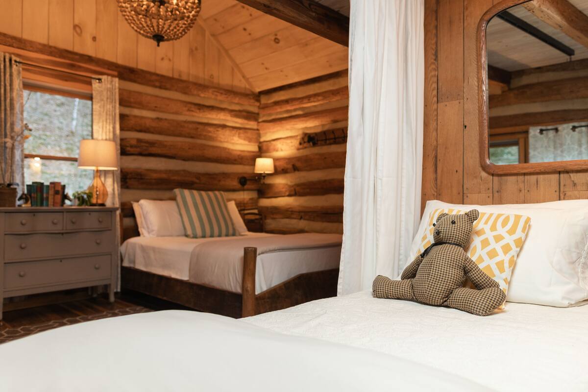 Un dormitorio acogedor tipo cabaña de madera con una cama, un aparador, un espejo y un osito de peluche sobre la cama.