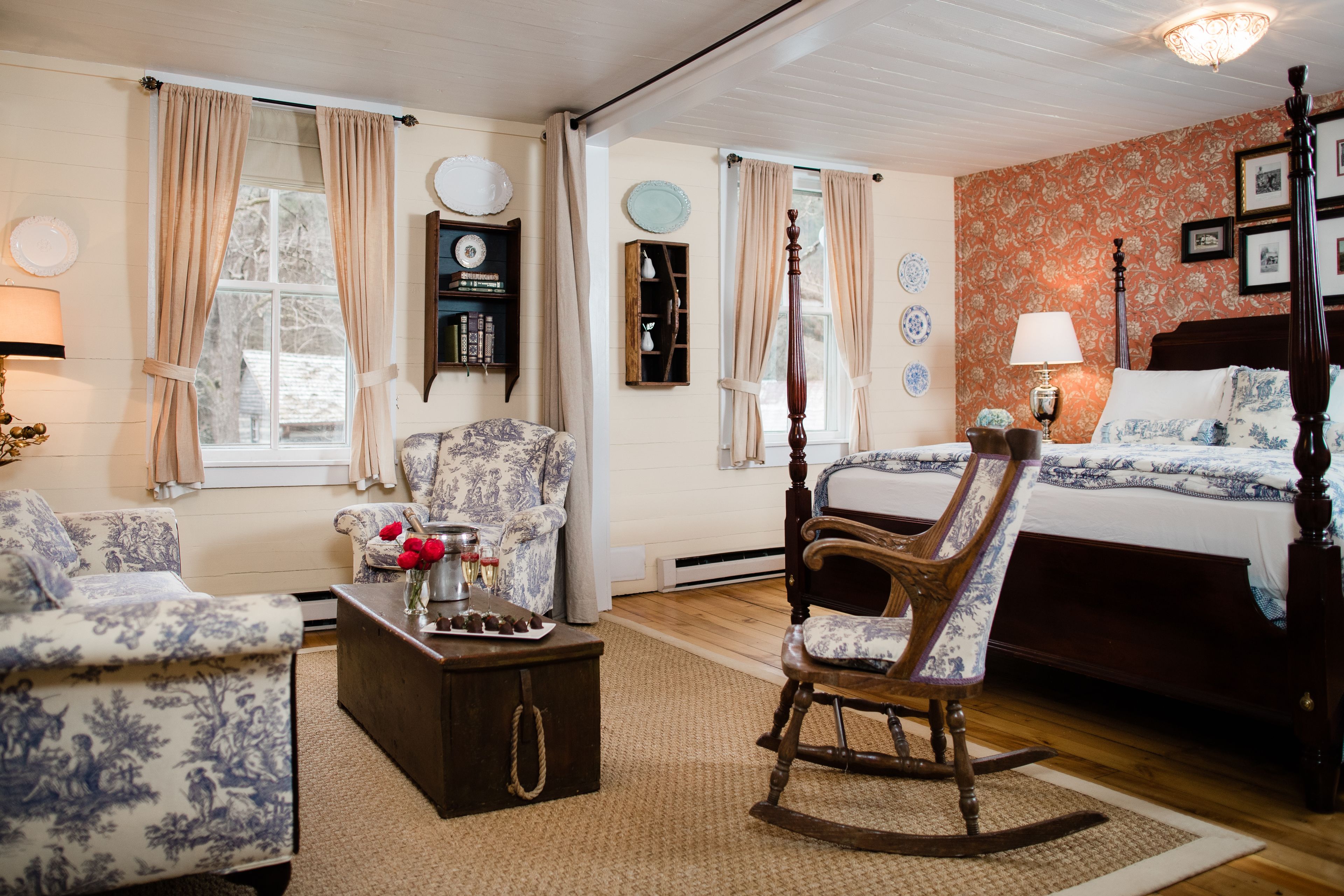 A bedroom with a four-poster bed, a rocking chair, a sofa, and a coffee table.