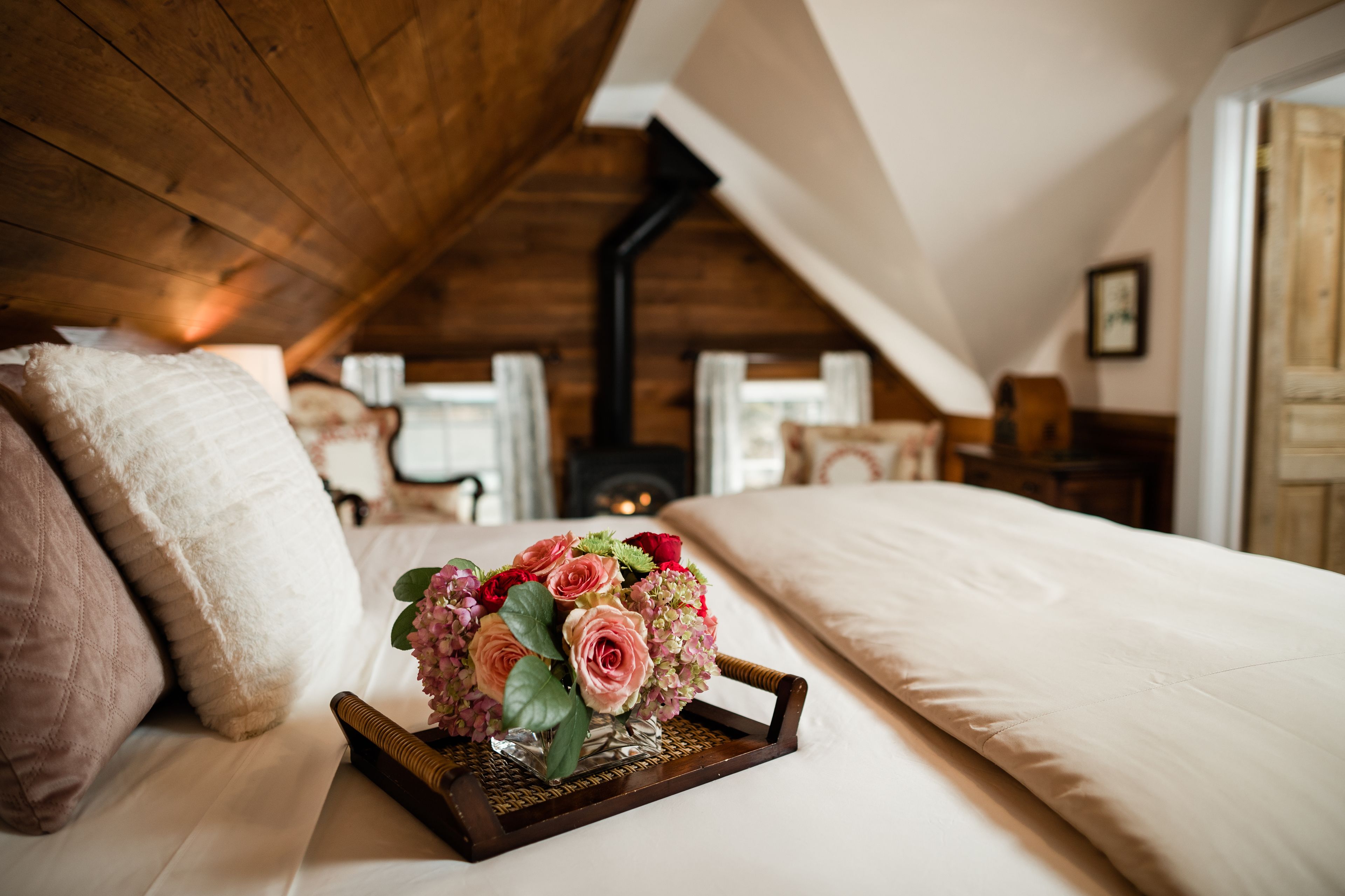 A cozy bedroom with a wooden ceiling, a bed with white bedding, and a bedside table with a vase of flowers.