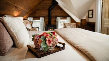 A cozy bedroom with a wooden ceiling, a bed with white bedding, and a bedside table with a vase of flowers.