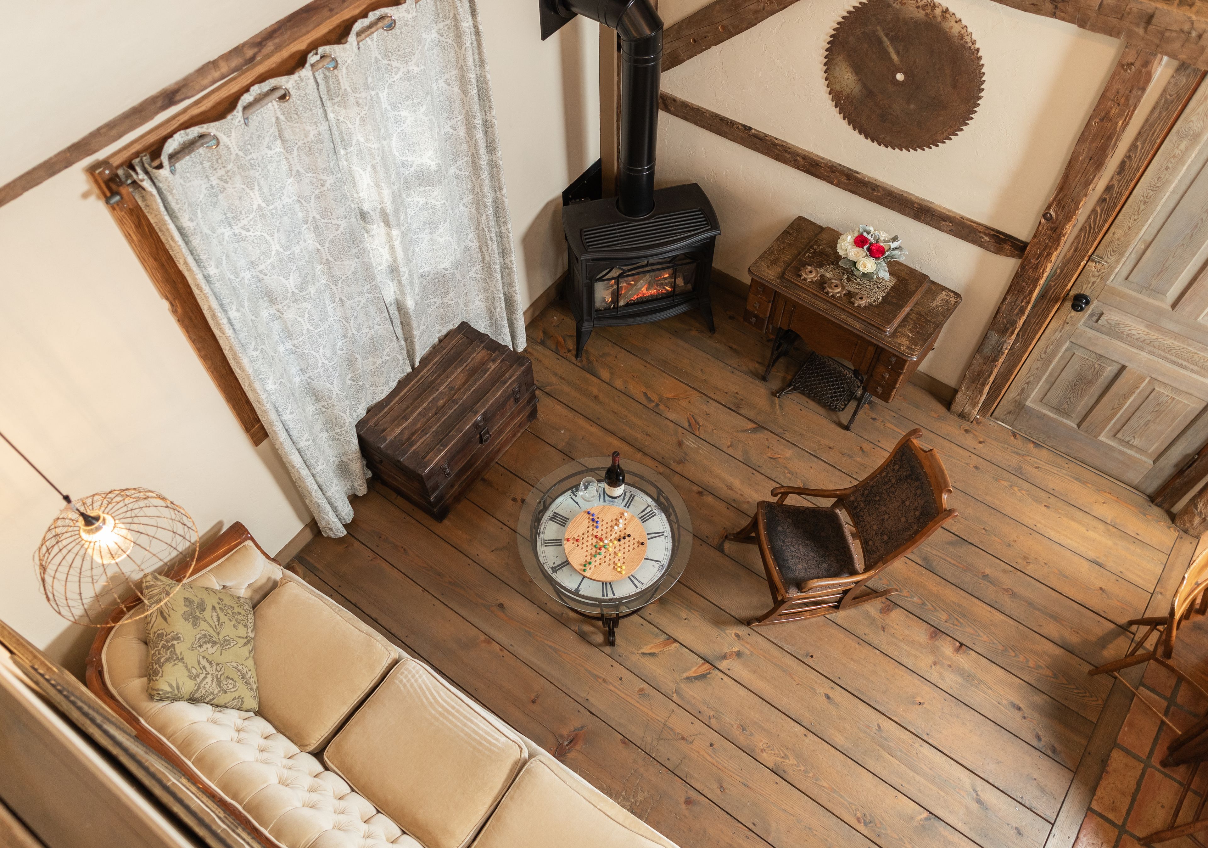 Una habitación acogedora con suelo de madera, un sofá, una mesa con un juego de mesa, una silla, una mesita con flores y una chimenea.